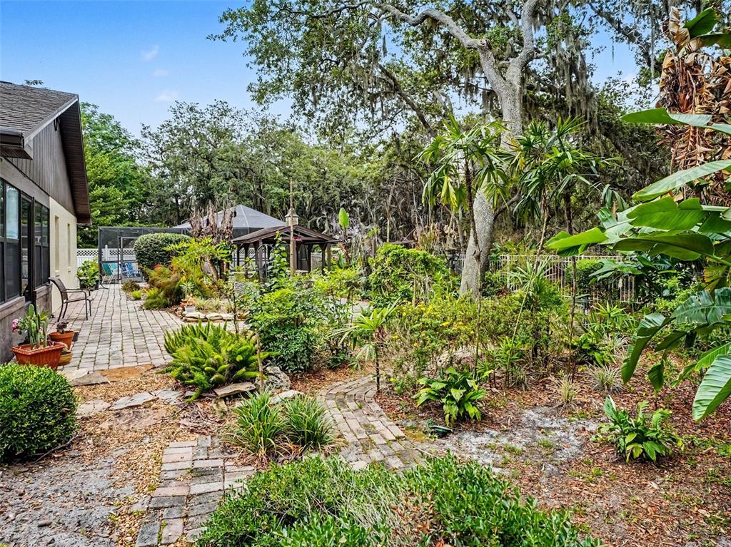 A brick patio and walkway lead through a lush, landscaped backyard with mature trees — 4870 CITRUS OAK LANE, ST CLOUD, FL