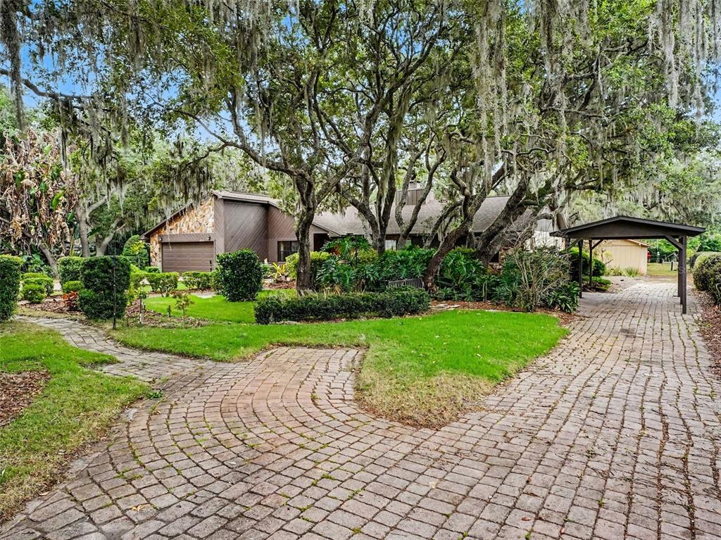 A brick driveway leads to a house with a carport and large, moss-covered oak trees — 4870 CITRUS OAK LANE, ST CLOUD, FL