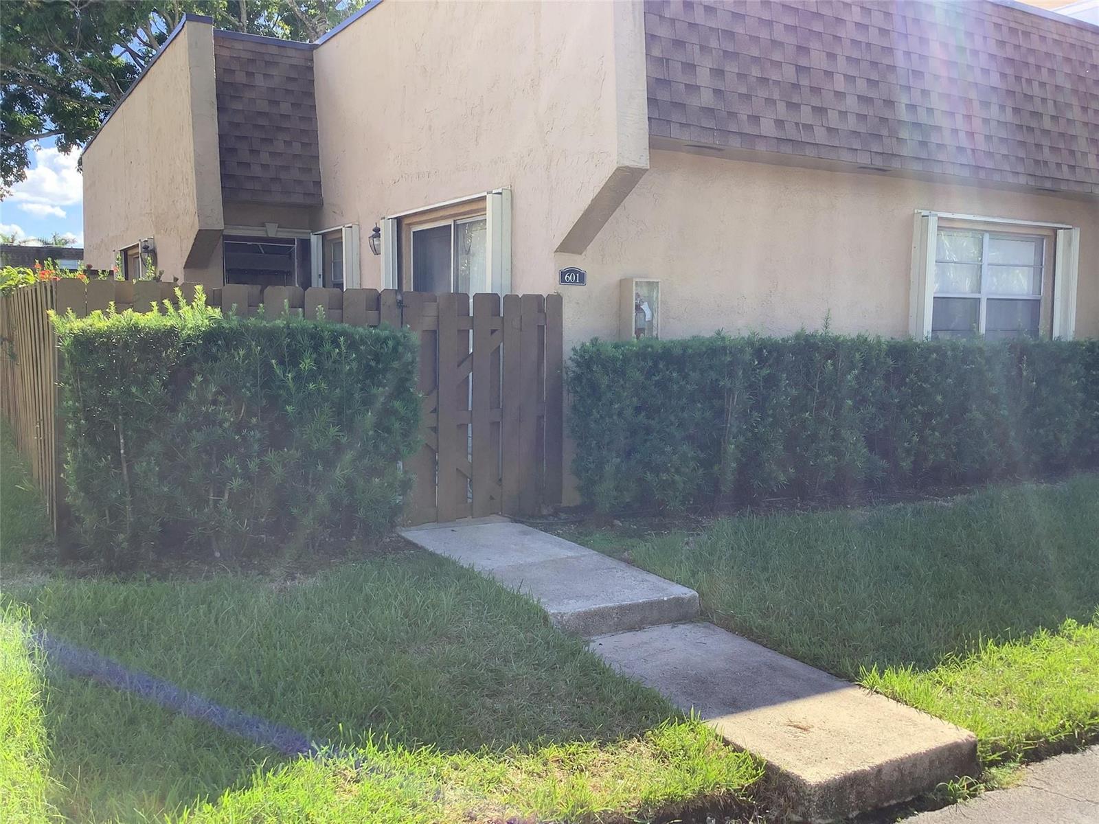 A tan townhouse exterior features a wooden privacy fence, a concrete walkway, and manicured hedges — 3581 NW 95th Terrace # 601, Sunrise FL 33351, SUNRISE, FL