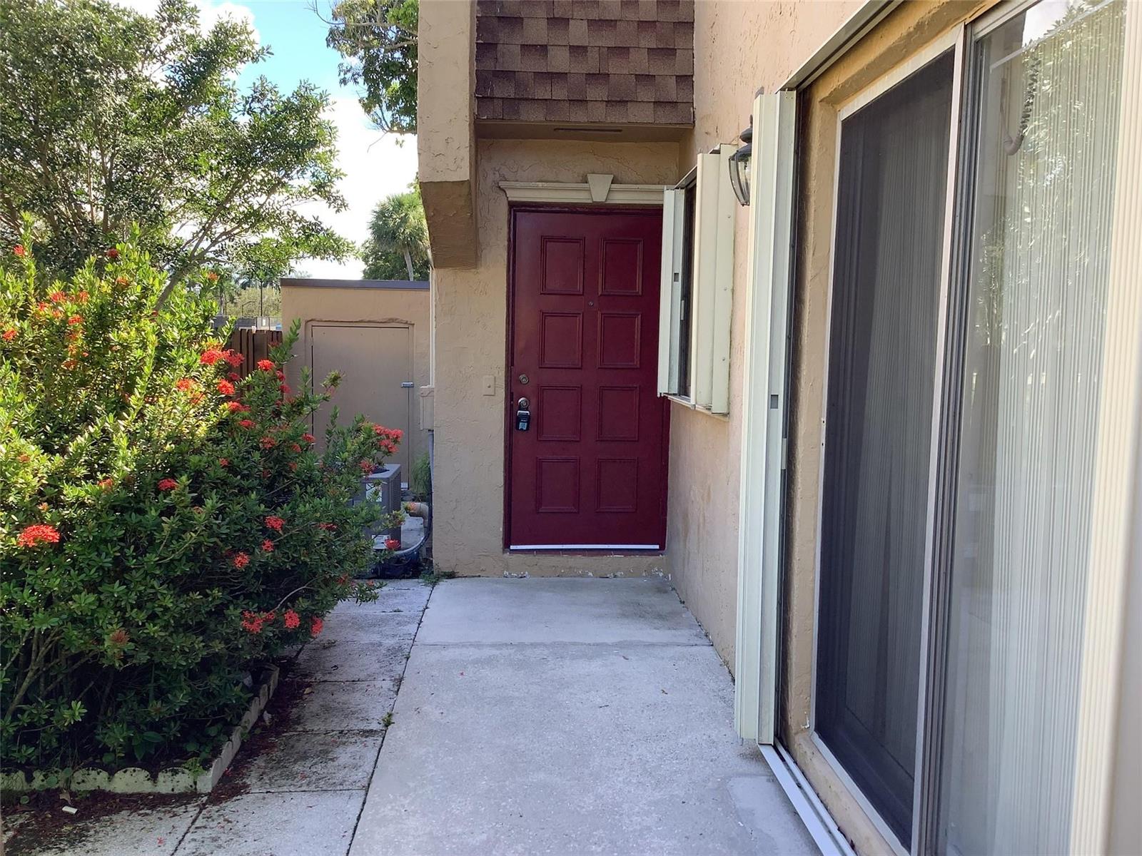 A red front door is situated on a concrete walkway next to a sliding glass door — 3581 NW 95th Terrace # 601, Sunrise FL 33351, SUNRISE, FL