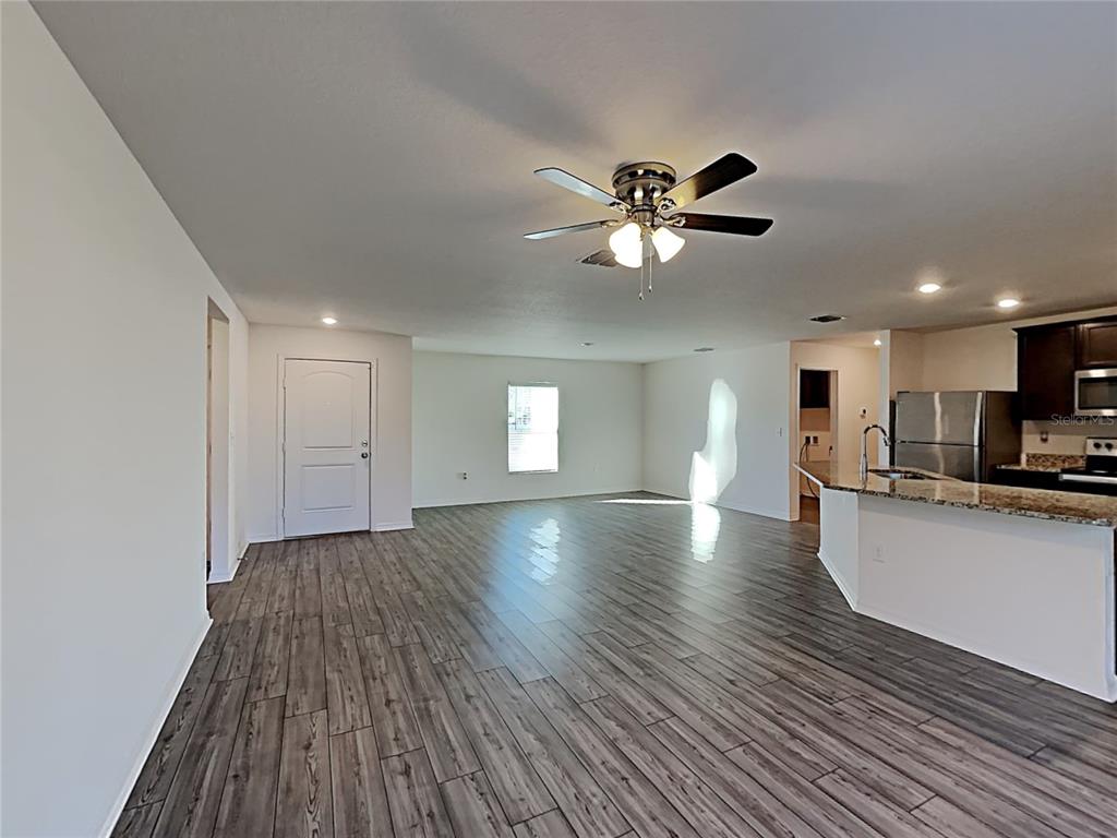 An open-concept living area with wood-look flooring, a ceiling fan, and an adjacent kitchen — 424 OHIO LANE, KISSIMMEE, FL