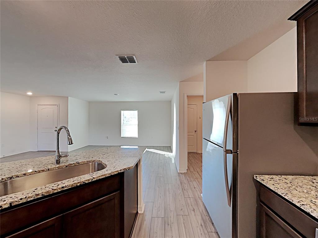 A kitchen with granite countertops and dark cabinets overlooks a living area with tile flooring — 424 OHIO LANE, KISSIMMEE, FL