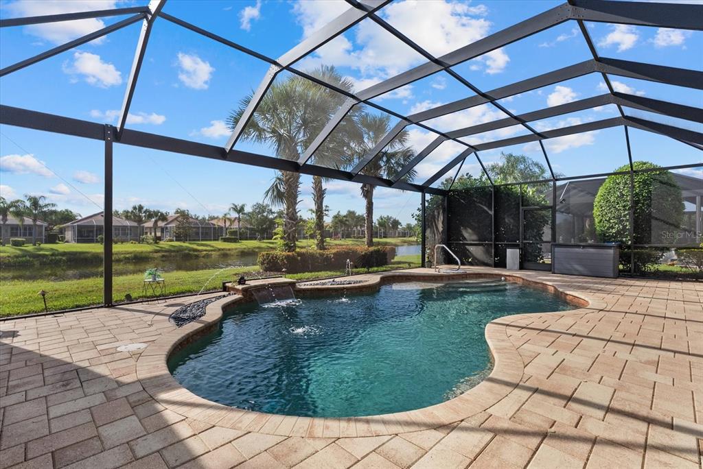 A screened-in patio features a freeform swimming pool with a water feature and pavers — 19168 JALISCA STREET, VENICE, FL