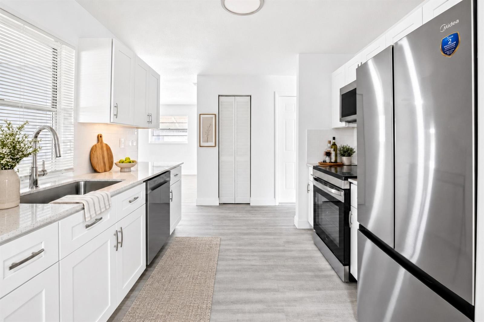 A bright, modern kitchen features white cabinets, stainless steel appliances, and light wood-look flooring — 703 SW 18th Street, Boynton Beach FL 33426, BOYNTON BEACH, FL
