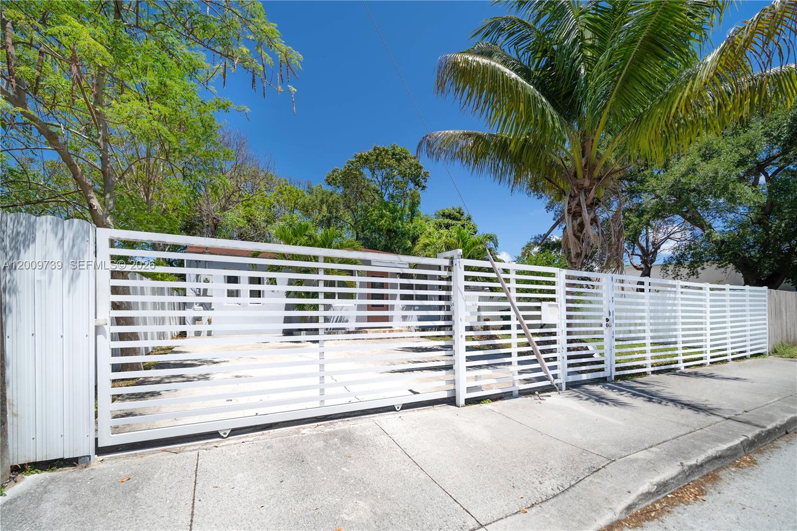 A white horizontal slat fence encloses a paved driveway in front of a house — 235 NW 59th St, Miami FL 33127, MIAMI, FL