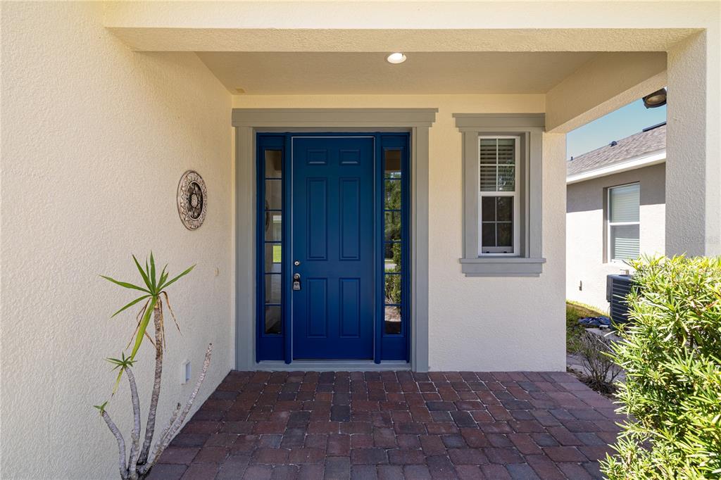 A blue front door with sidelights sits under a covered porch with brick pavers — 6023 W TOWN CENTER BOULEVARD, ORLANDO, FL