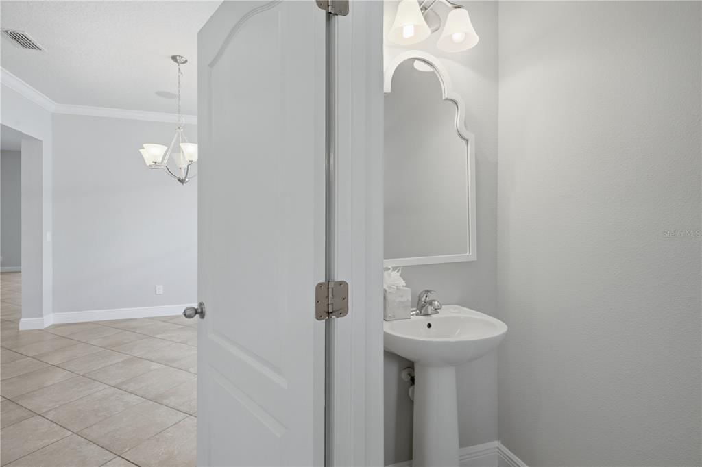 A pedestal sink and a decorative mirror are inside a small bathroom next to a hallway — 6023 W TOWN CENTER BOULEVARD, ORLANDO, FL