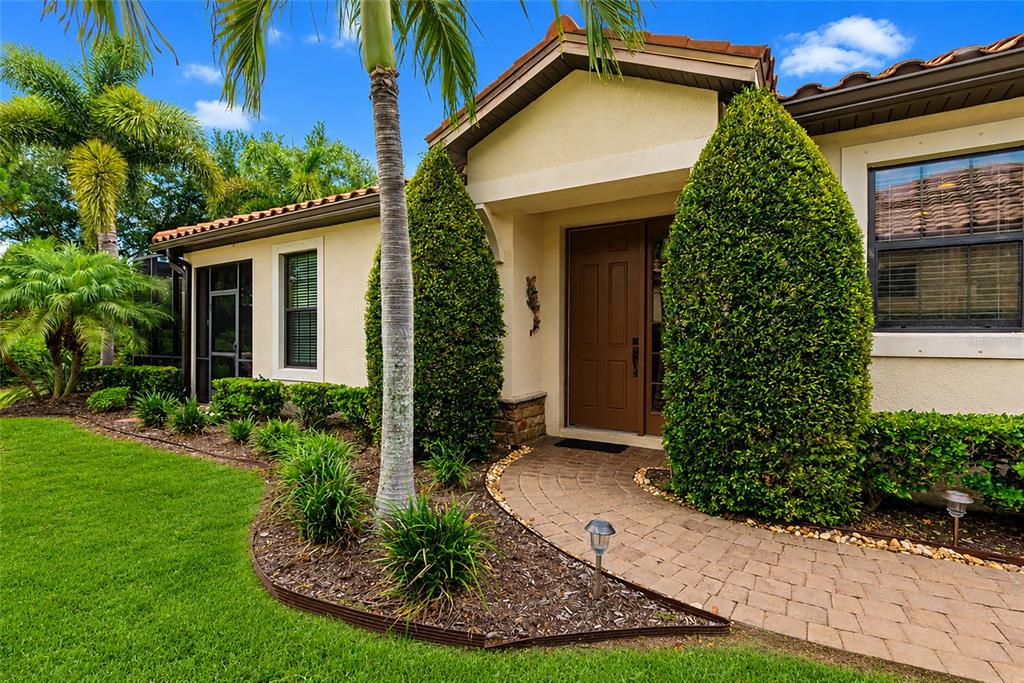 The exterior of a house features a brown front door, a brick walkway, and landscaping — 5126 SAVONA RUN, BRADENTON, FL