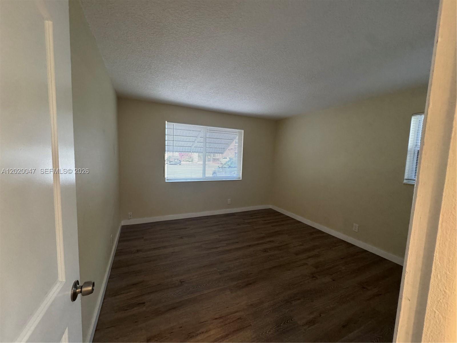 An empty bedroom features light-colored walls, dark wood-look flooring, and two windows with blinds — 707 S 19th Ave # 2, Hollywood FL 33020, HOLLYWOOD, FL