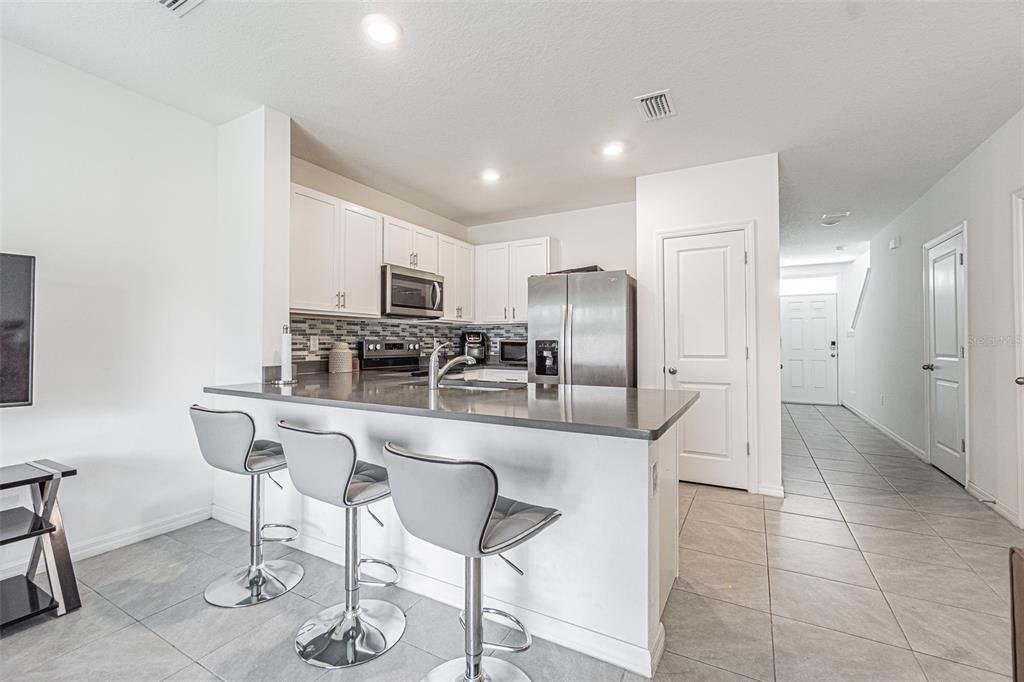 A kitchen features white cabinets, stainless steel appliances, a gray island, and three bar stools — 6358 SOPHIE OAKS COURT, TAMPA, FL