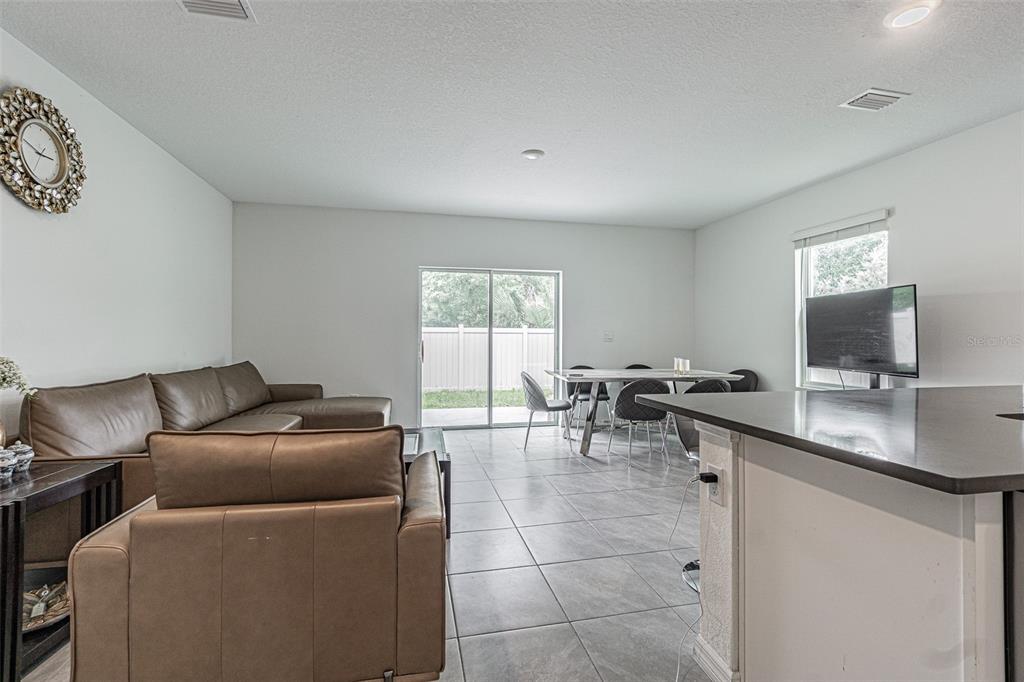 An open-concept living and dining area features tile flooring, leather furniture, and a sliding door — 6358 SOPHIE OAKS COURT, TAMPA, FL