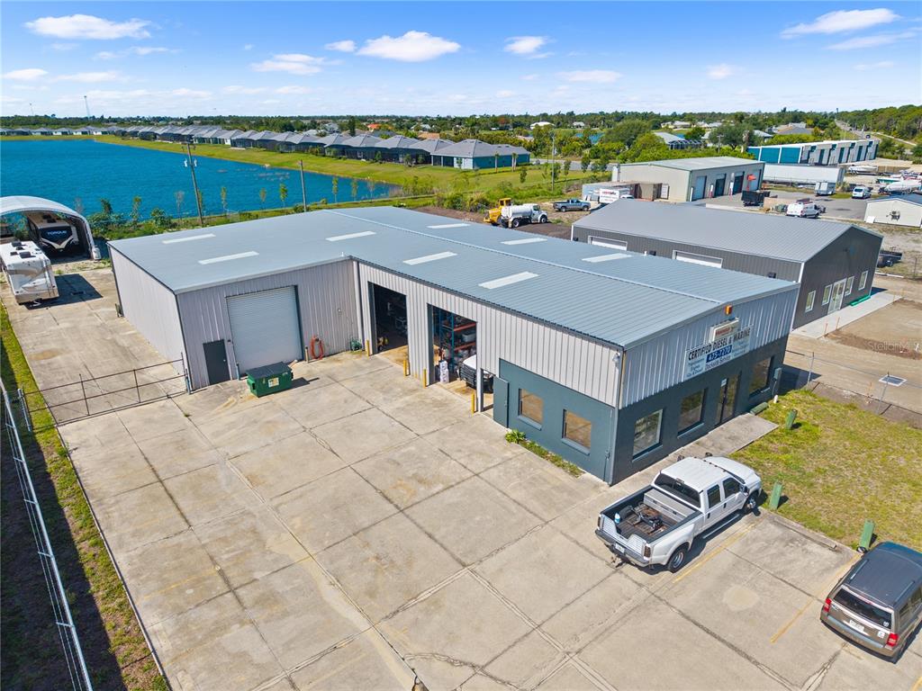 An aerial view shows a metal industrial building with a concrete parking lot and lake — 2640 AVENUE OF THE AMERICAS, ENGLEWOOD, FL