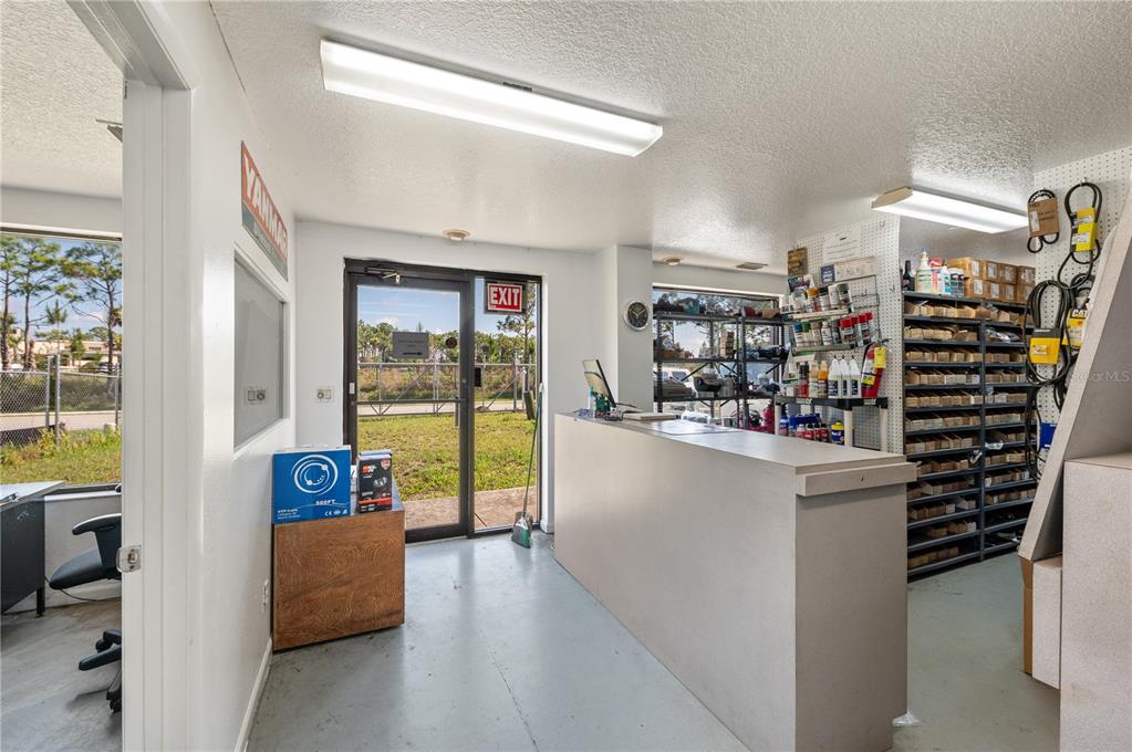 A commercial office space features a service counter, storage shelving, and a glass exit door — 2640 AVENUE OF THE AMERICAS, ENGLEWOOD, FL