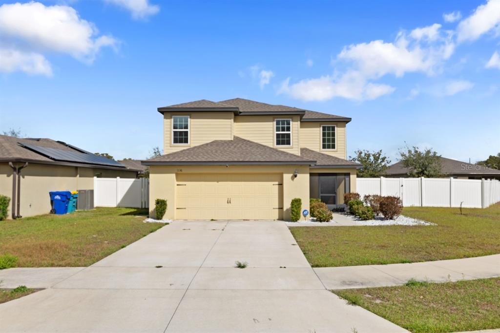 A two-story, tan-colored suburban house features a two-car garage and a concrete driveway — 1136 SEA PINES COURT, TAVARES, FL