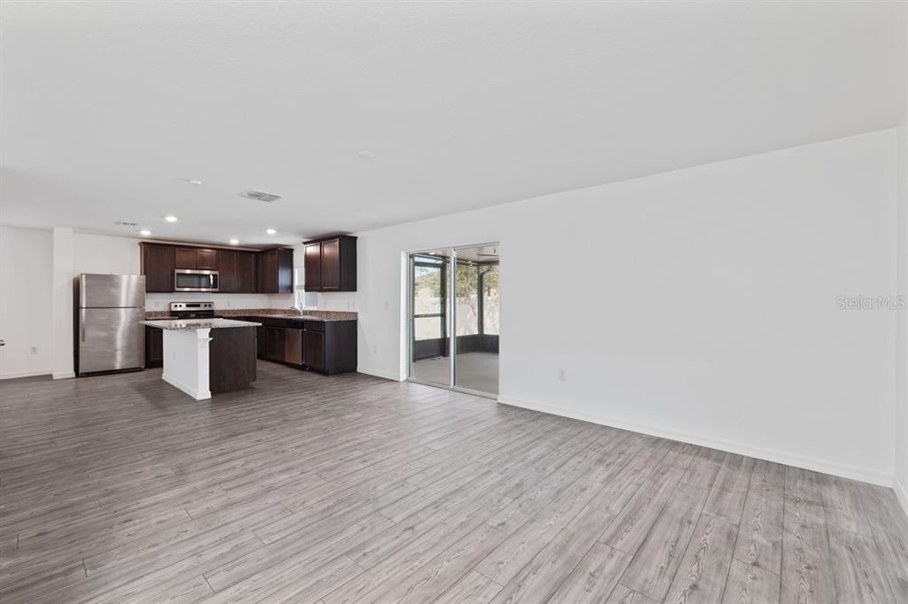 An open-concept living area features wood-look flooring, a kitchen with dark cabinets, and sliding doors — 1136 SEA PINES COURT, TAVARES, FL
