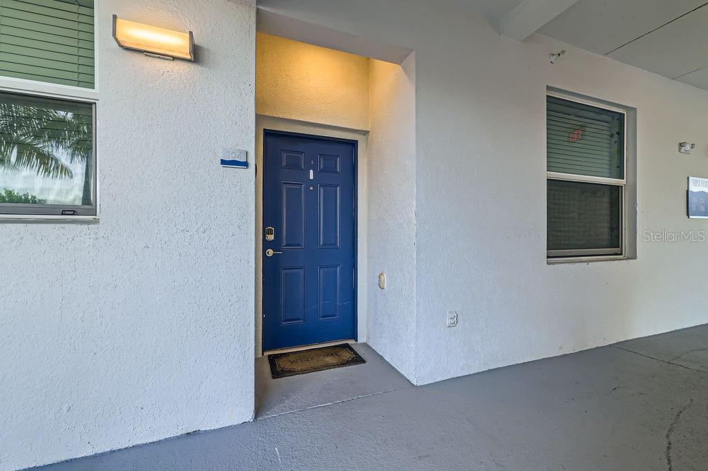A blue front door is set into a white stucco exterior wall with a window — 4731 CLOCK TOWER DRIVE UNIT 104, KISSIMMEE, FL