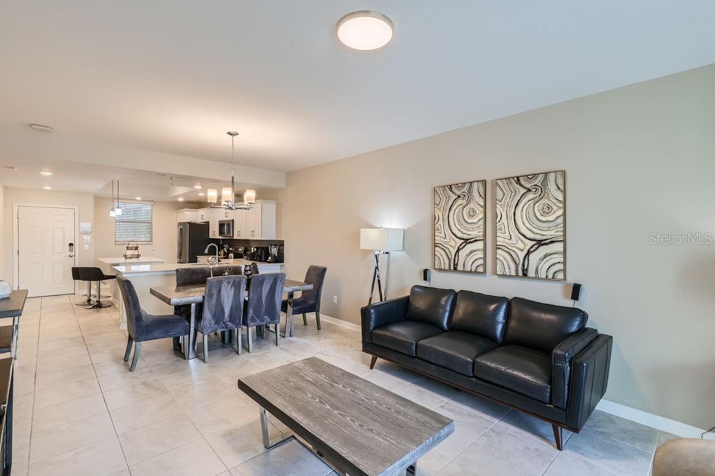 An open-concept living and dining area features tile flooring, a black sofa, and a kitchen — 4731 CLOCK TOWER DRIVE UNIT 104, KISSIMMEE, FL
