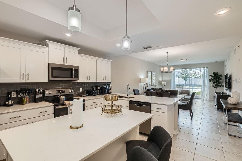 A modern kitchen with white cabinets, a large island, and stainless steel appliances overlooks a living area — 4731 CLOCK TOWER DRIVE UNIT 104, KISSIMMEE, FL