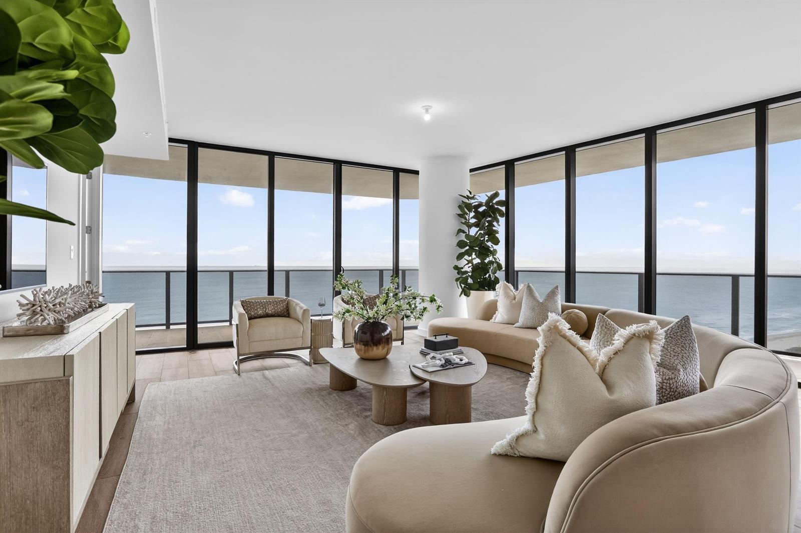 A modern living room features a curved sofa, coffee tables, and floor-to-ceiling ocean views — 900 N Ocean Boulevard # 1401, Pompano Beach FL 33062, POMPANO BEACH, FL