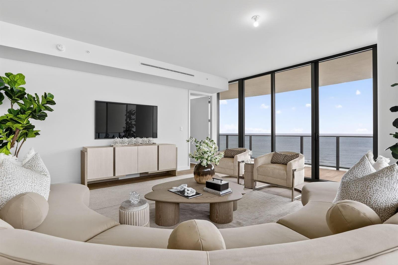 A modern living room features a curved sofa, coffee table, and floor-to-ceiling windows overlooking the ocean — 900 N Ocean Boulevard # 1401, Pompano Beach FL 33062, POMPANO BEACH, FL