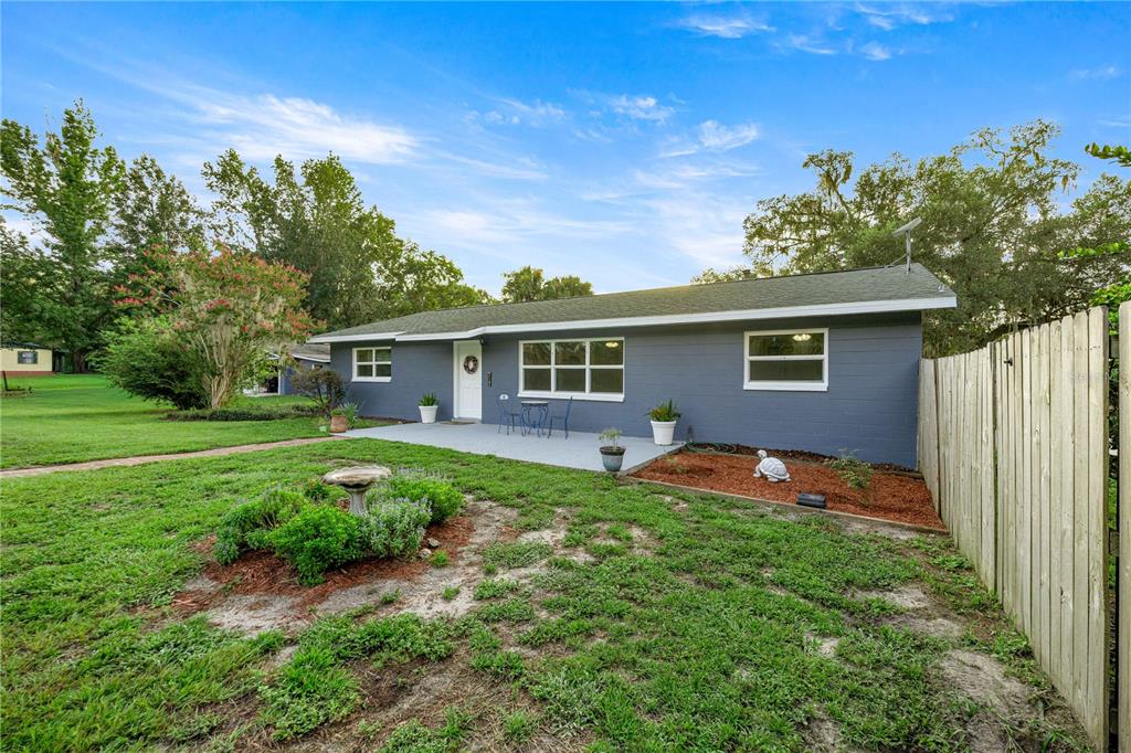A single-story gray house with a concrete patio, a white door, and a wooden fence — 15027 SW 91ST STREET, ARCHER, FL