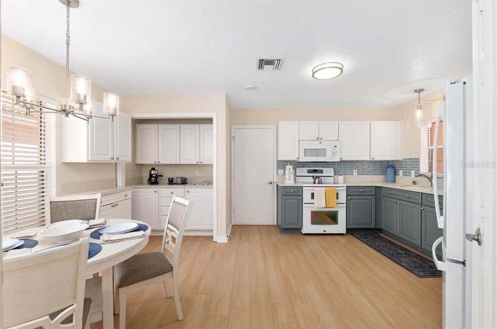 A kitchen and dining area with white upper cabinets, grey lower cabinets, and light wood flooring — 1305 SANTA MARIA AVENUE, LADY LAKE, FL