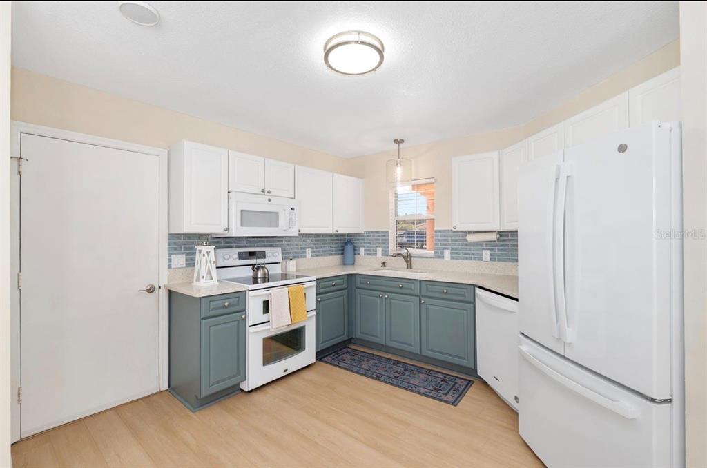 A kitchen with white upper cabinets, blue lower cabinets, white appliances, and a tiled backsplash — 1305 SANTA MARIA AVENUE, LADY LAKE, FL