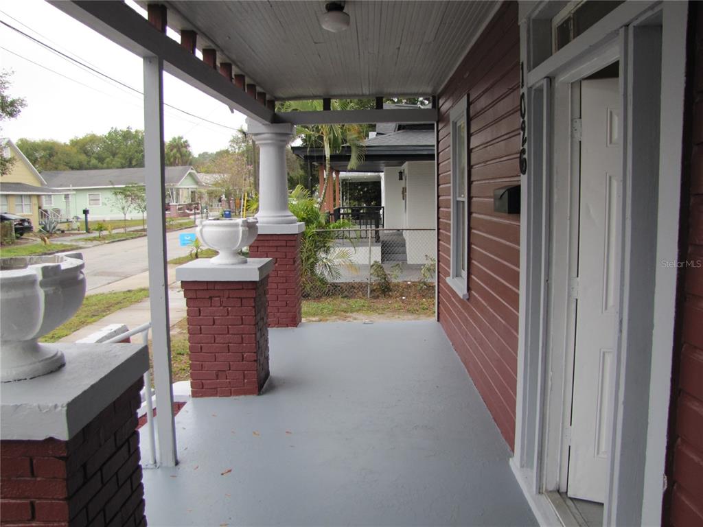 A covered front porch features red brick columns, white pillars, and a gray painted floor — 1026 E 15TH AVENUE, TAMPA, FL