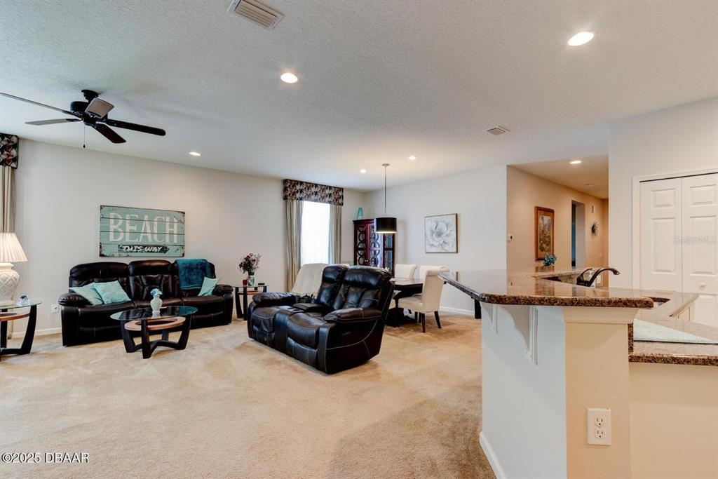 A living room and dining area feature carpeted floors, leather furniture, and a kitchen island — 145 PRESTWICK GRANDE DRIVE, DAYTONA BEACH, FL