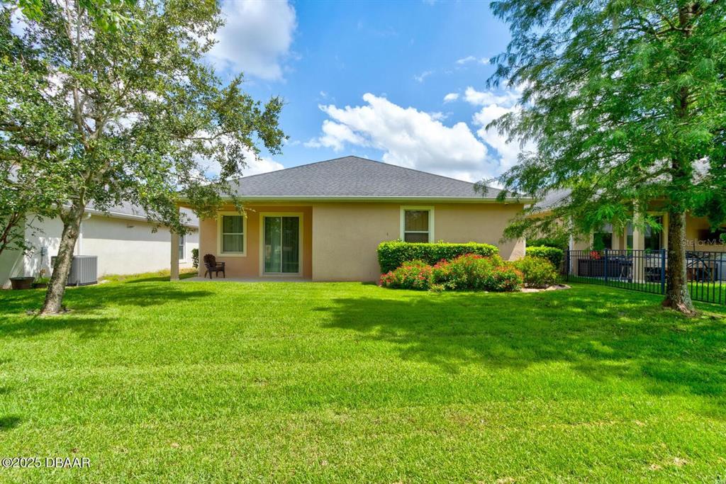 The back exterior of a tan house features a small patio and a grassy yard — 145 PRESTWICK GRANDE DRIVE, DAYTONA BEACH, FL