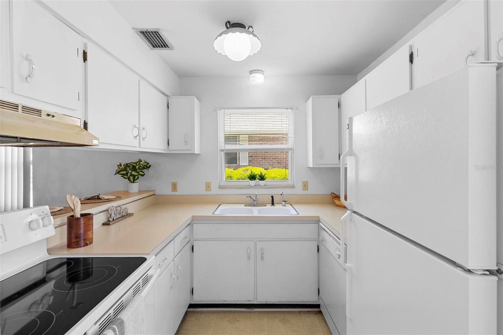 A galley kitchen features white cabinets, tan countertops, a white refrigerator, and a window — 3 FAIRWAY COURT, DELAND, FL
