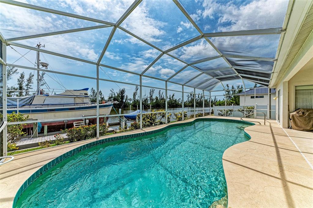 A screened-in pool patio overlooks a canal with a docked boat — 10640 AYEAR ROAD, PORT CHARLOTTE, FL