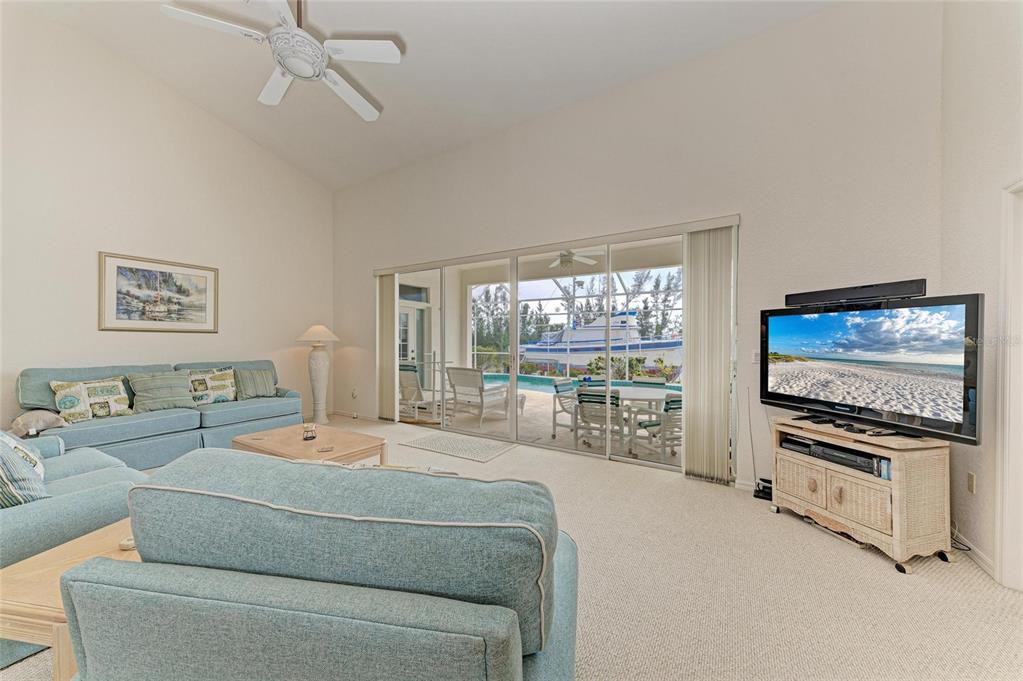 A living room with light blue sofas, a television, and sliding doors opening to a pool — 10640 AYEAR ROAD, PORT CHARLOTTE, FL