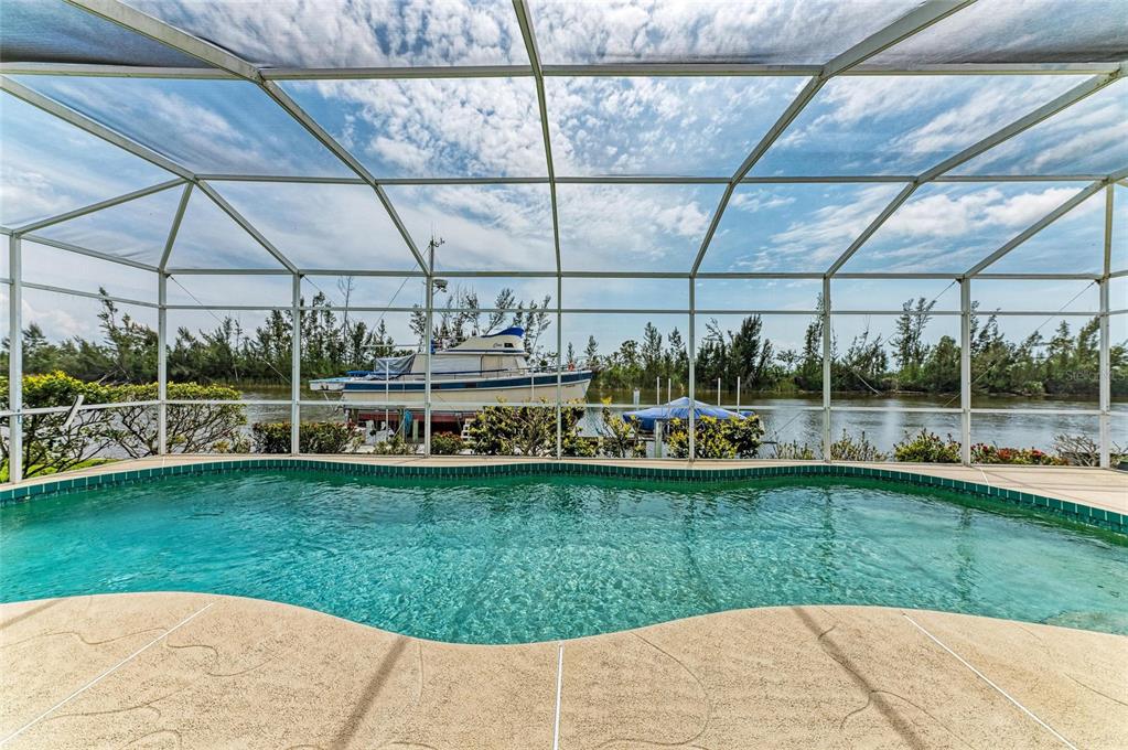A screened-in swimming pool overlooks a canal with a docked boat and lush vegetation — 10640 AYEAR ROAD, PORT CHARLOTTE, FL