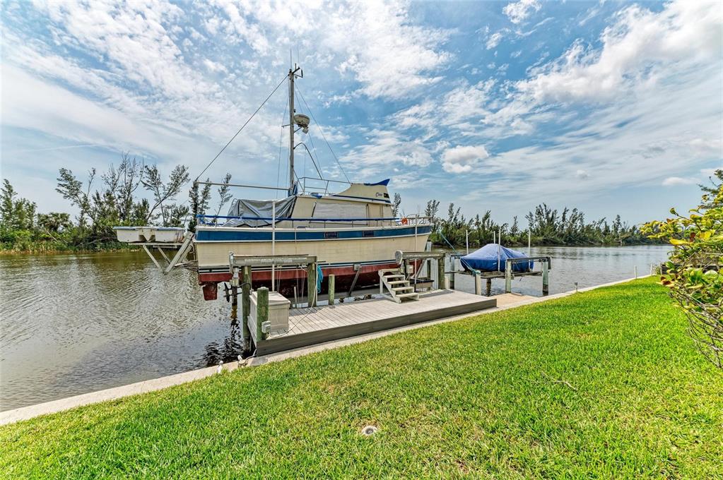 A boat is docked on a lift next to a wooden pier along a grassy canal — 10640 AYEAR ROAD, PORT CHARLOTTE, FL