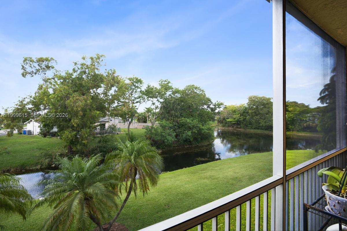 A view from a screened balcony overlooking a grassy lawn, a pond, and trees — 6870 Royal Palm Blvd # 209M, Margate FL 33063, MARGATE, FL