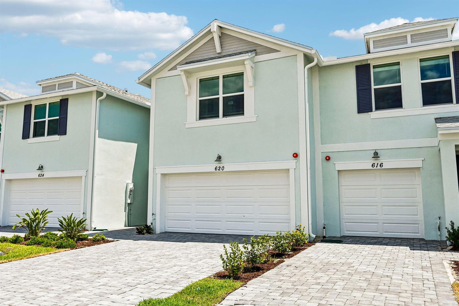 Three light green townhouses with white garage doors and paved driveways stand under a blue sky — 620 Salisbury Circle, Fort Pierce FL 34982, FORT PIERCE, FL