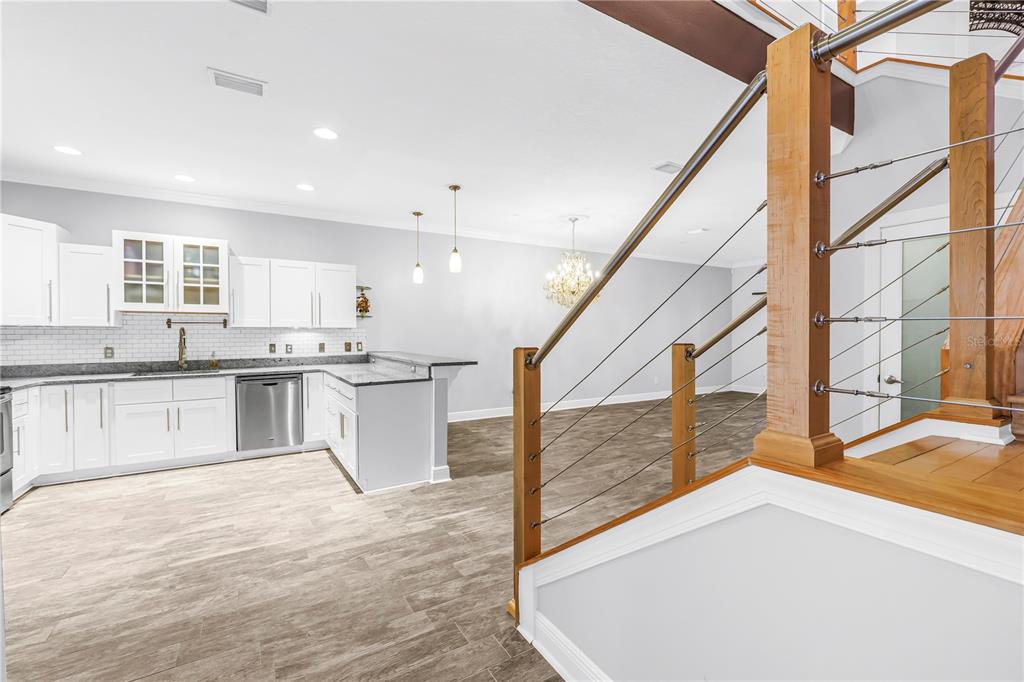 A kitchen with white cabinets and granite countertops overlooks a living area with wood flooring — 409 BARCELONA DRIVE, ST PETERSBURG, FL