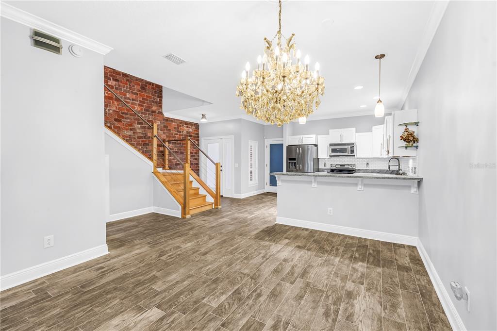 An open-concept room features wood-look tile flooring, a brick accent wall, and a crystal chandelier — 409 BARCELONA DRIVE, ST PETERSBURG, FL
