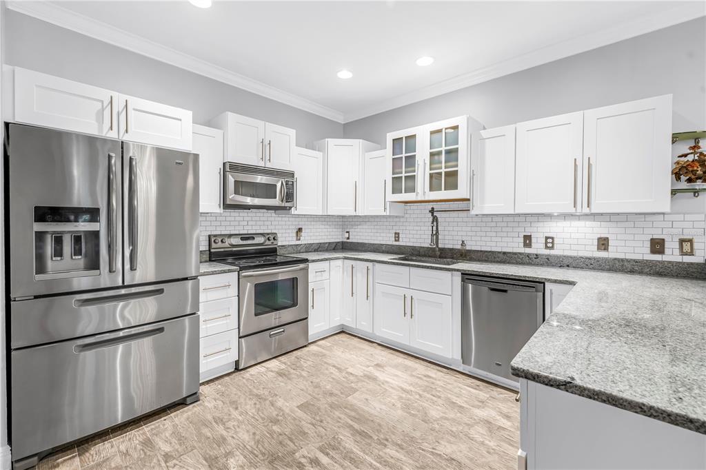 A kitchen with white cabinets, stainless steel appliances, granite countertops, and light wood-look flooring — 409 BARCELONA DRIVE, ST PETERSBURG, FL