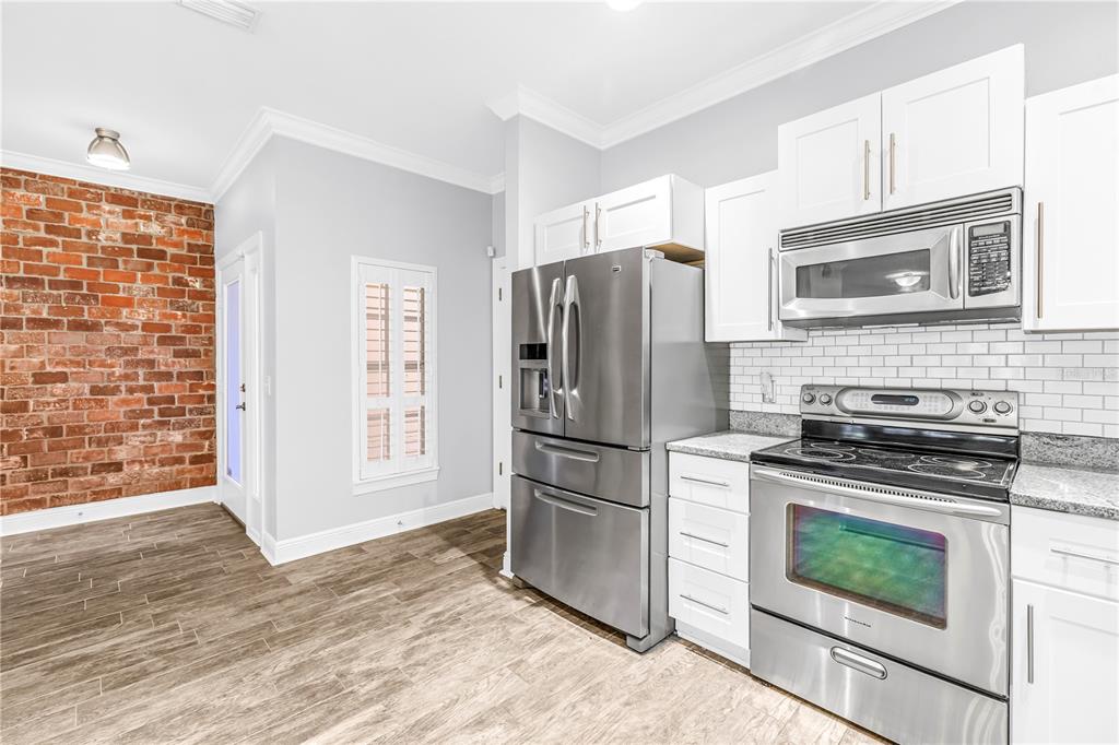 A kitchen with stainless steel appliances, white cabinets, granite countertops, and an exposed brick wall — 409 BARCELONA DRIVE, ST PETERSBURG, FL