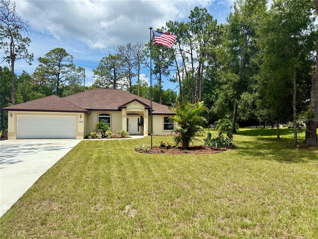 A single-story house with a two-car garage and an American flag in the front yard — 19939 SW 96TH PLACE, DUNNELLON, FL