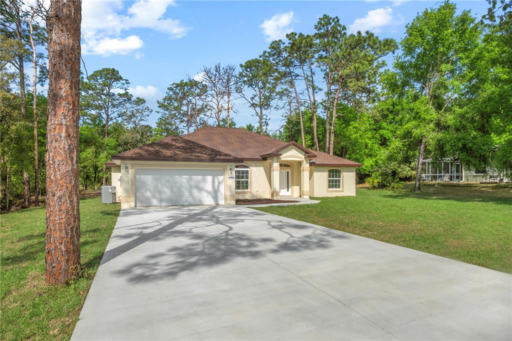 A single-story house with a beige stucco exterior, brown roof, and a concrete driveway — 19939 SW 96TH PLACE, DUNNELLON, FL