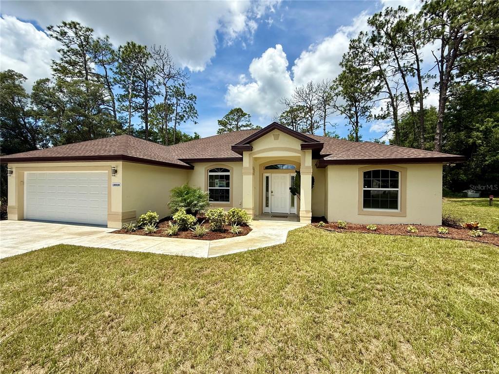 A single-story house with a two-car garage, tan stucco exterior, and a brown shingled roof — 19939 SW 96TH PLACE, DUNNELLON, FL