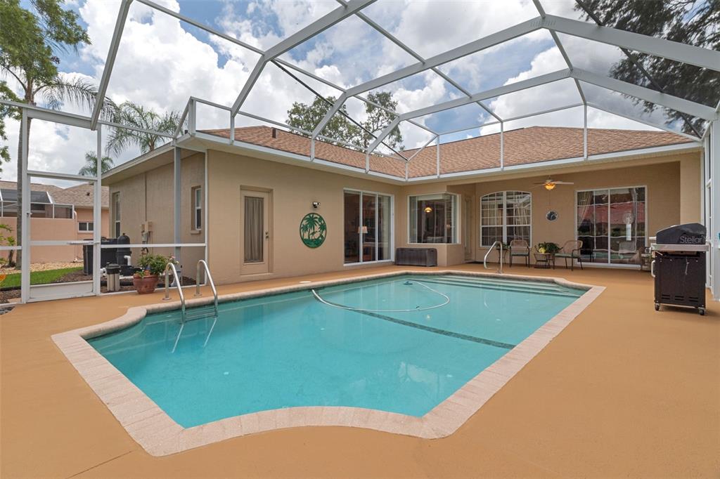A screened-in swimming pool with a tan deck sits behind a beige house — 13475 PRINCEWOOD COURT, SPRING HILL, FL