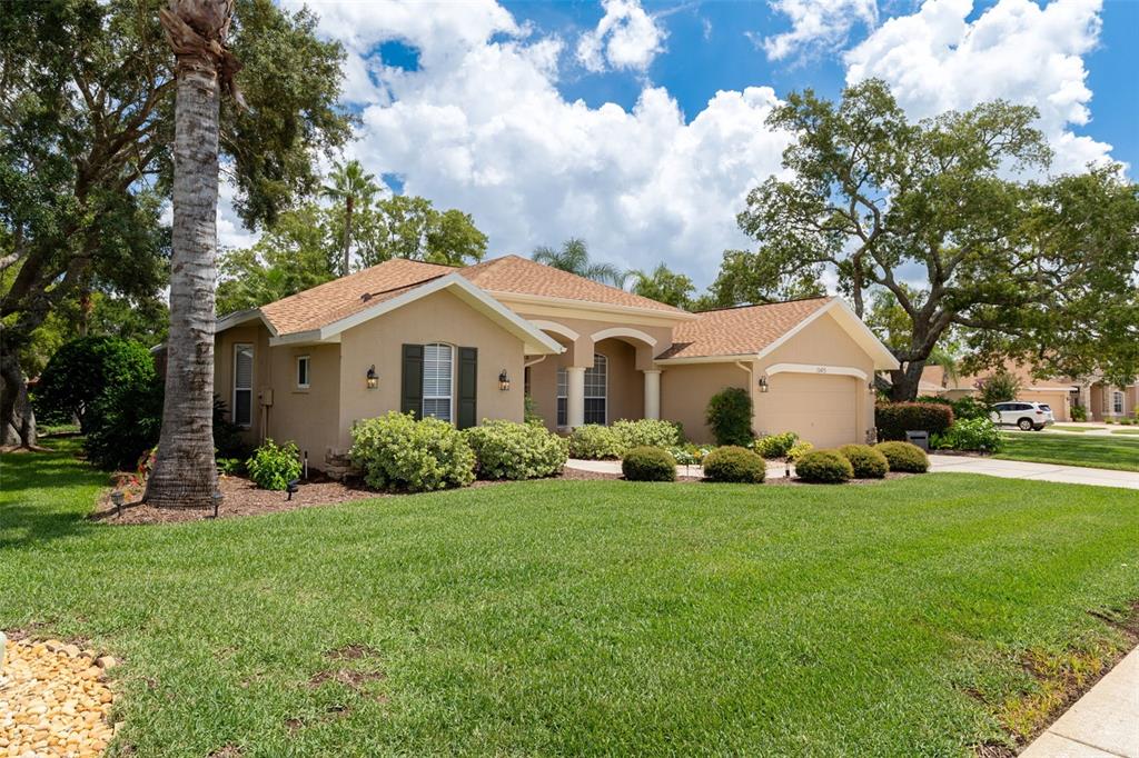 A single-story tan house with a brown shingled roof and a manicured front lawn — 13475 PRINCEWOOD COURT, SPRING HILL, FL