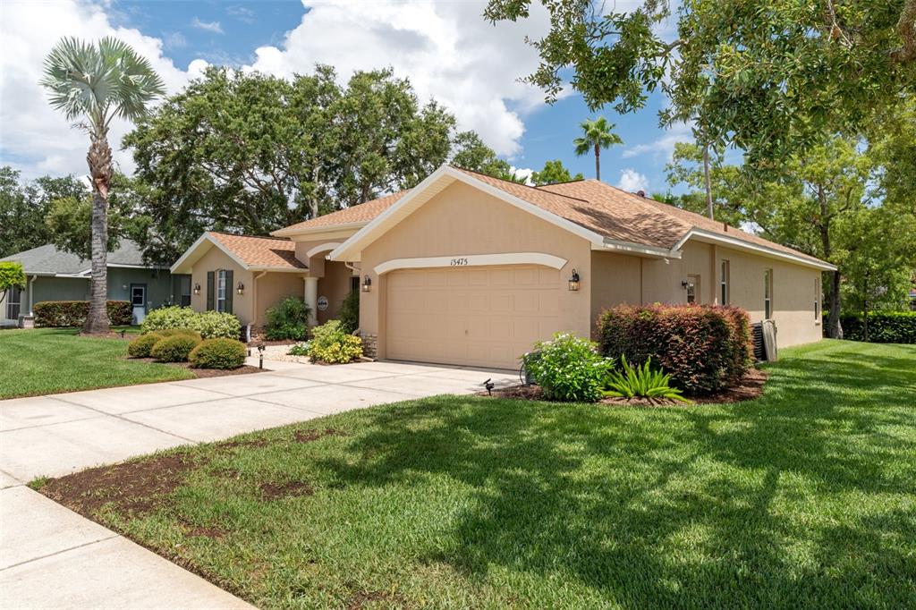 A tan single-story house with a two-car garage and a landscaped front yard — 13475 PRINCEWOOD COURT, SPRING HILL, FL
