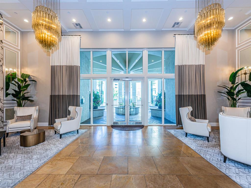 A grand lobby features two large crystal chandeliers, floor-to-ceiling windows, and four white armchairs — 11 BAYMONT STREET UNIT 403, CLEARWATER BEACH, FL