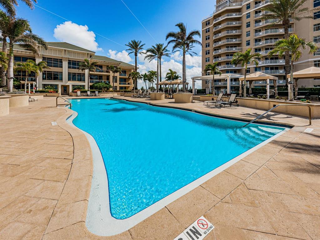 A large, free-form swimming pool is surrounded by a tan stone deck and palm trees — 11 BAYMONT STREET UNIT 403, CLEARWATER BEACH, FL