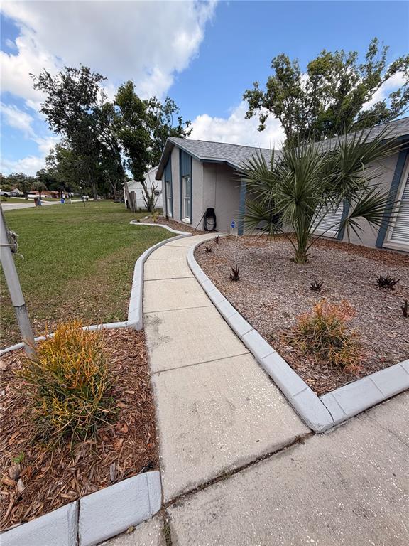 A concrete walkway leads to the entrance of a house with gray siding and landscaping — 1210 LADY ELAINE DRIVE, VALRICO, FL